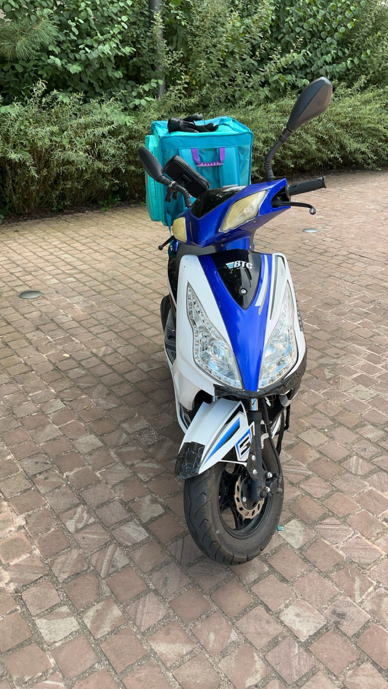 Mon scooter stationné à l’ombre, prêt pour une livraison avec le sac Deliveroo